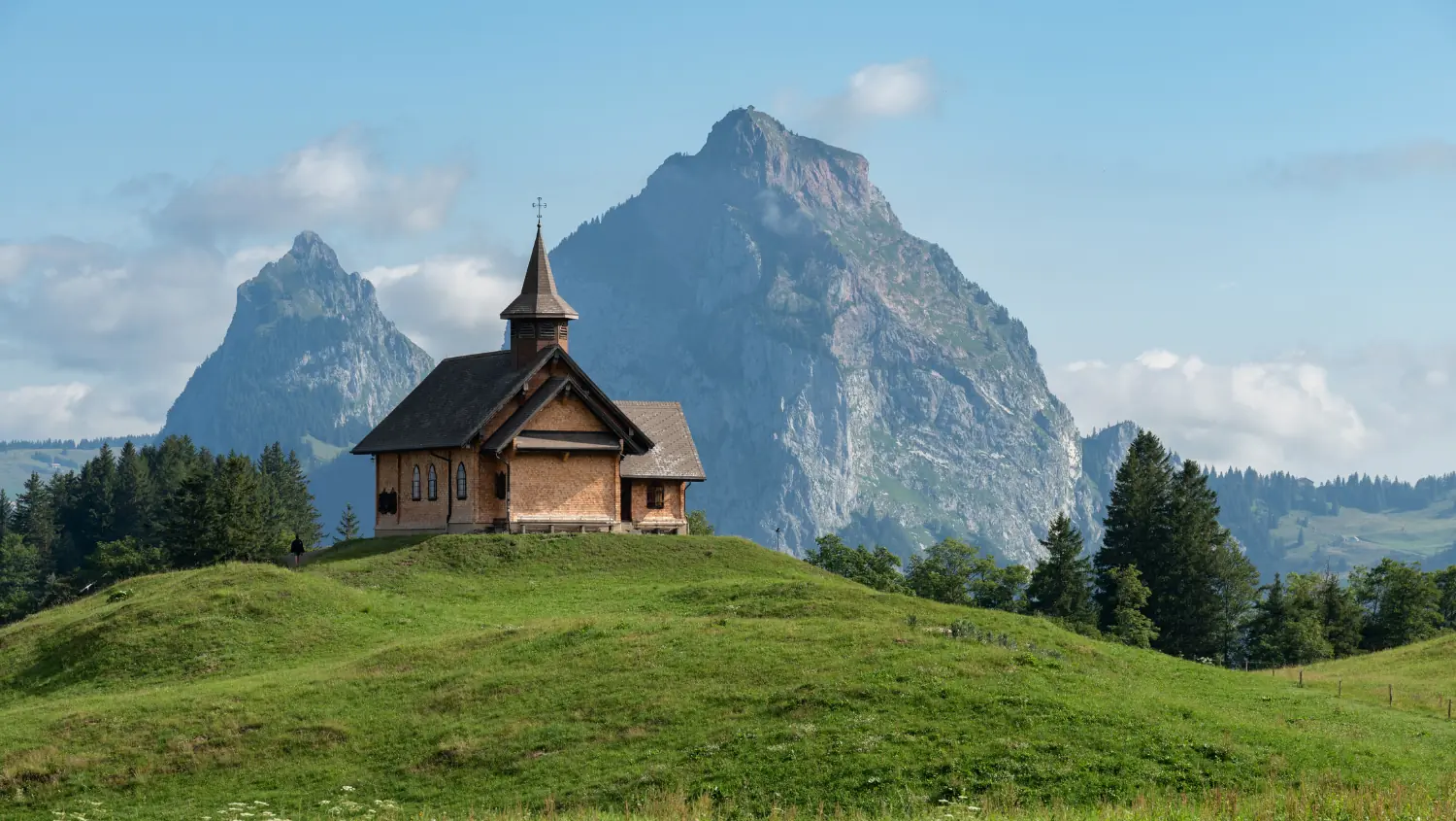 Holzkapelle auf einer Wiese beim Stoos, dahinter ein markanter Felsgipfel