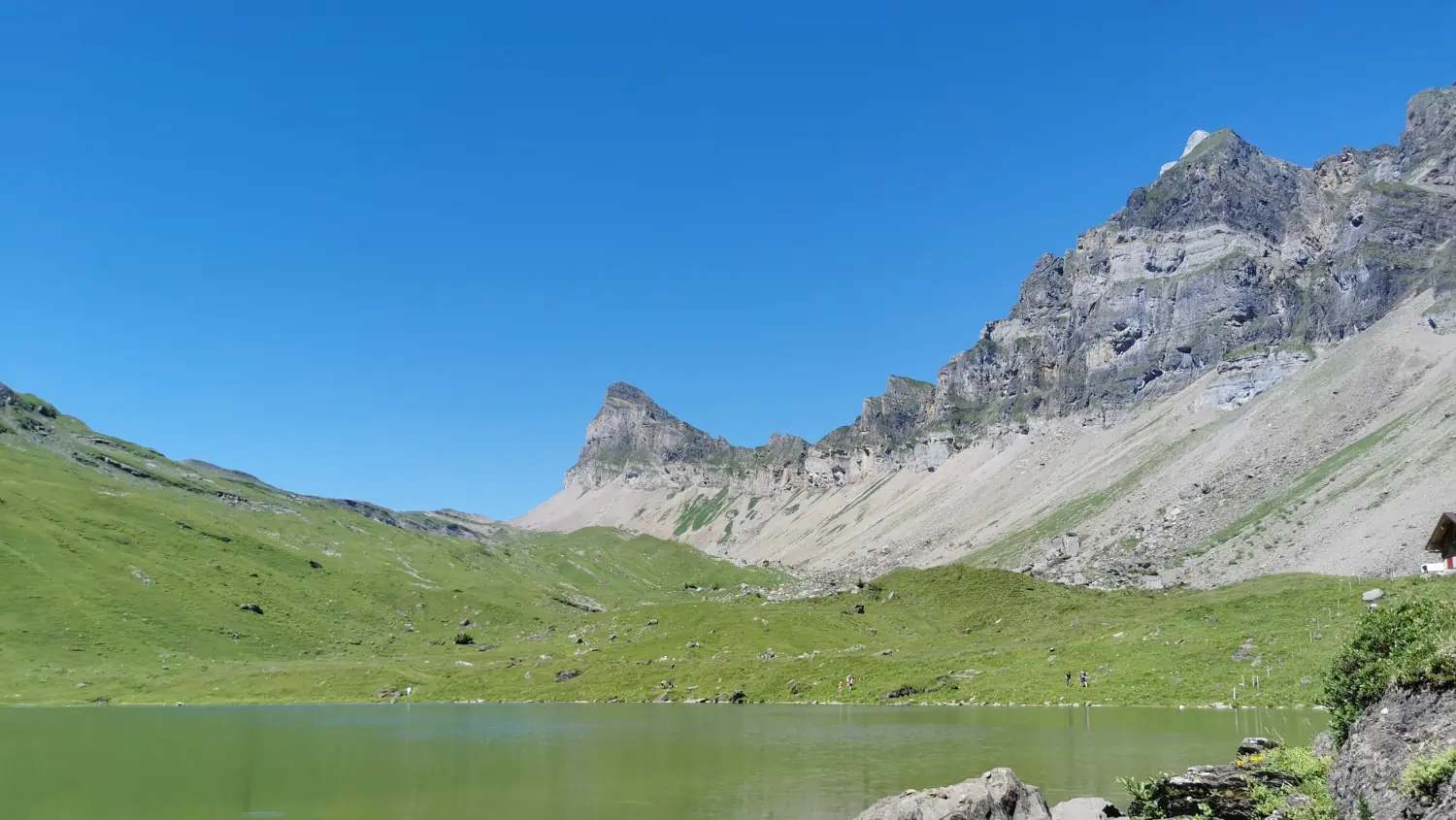 Lac de montagne turquoise sous une paroi rocheuse, un sentier le long de la rive