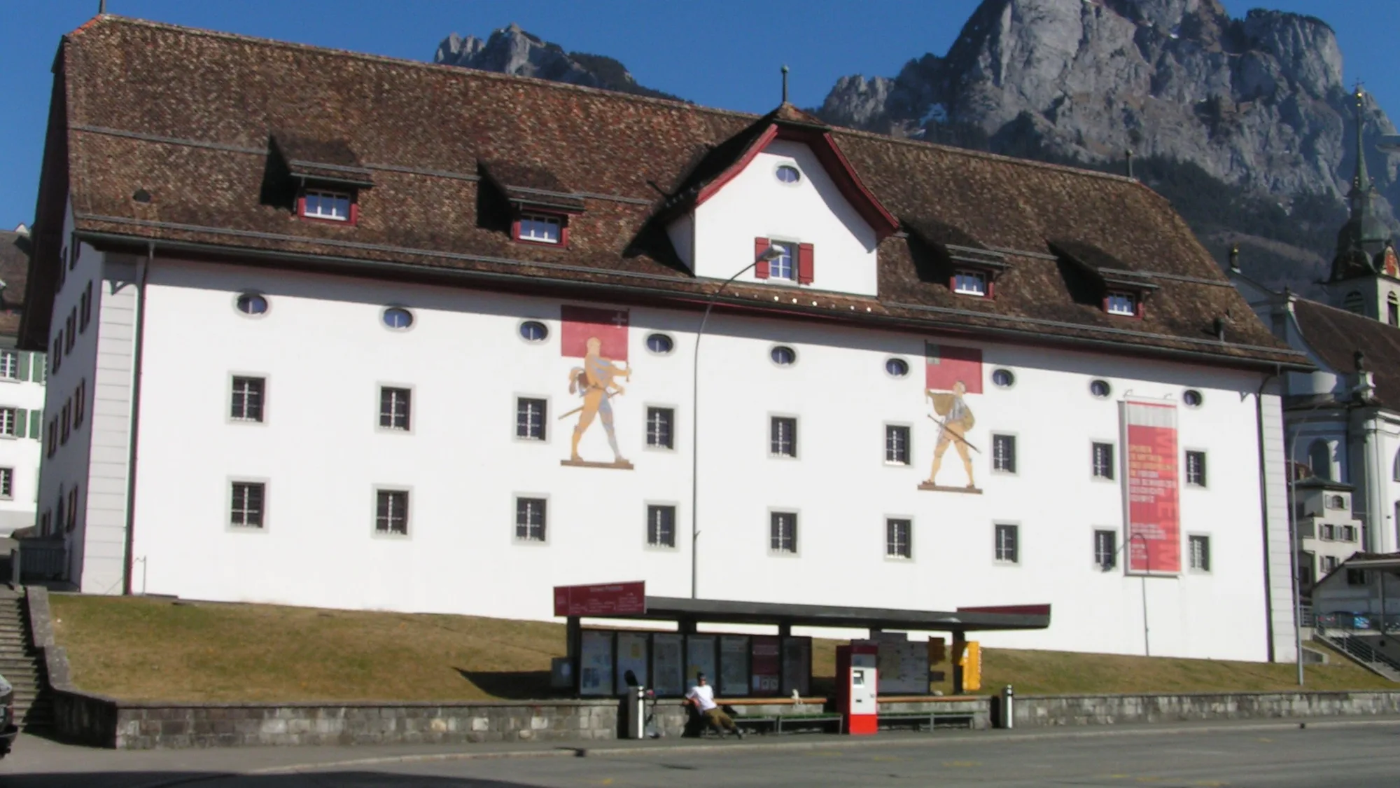 The white Forum of Swiss History with red shutters in Schwyz, behind it the two Mythen