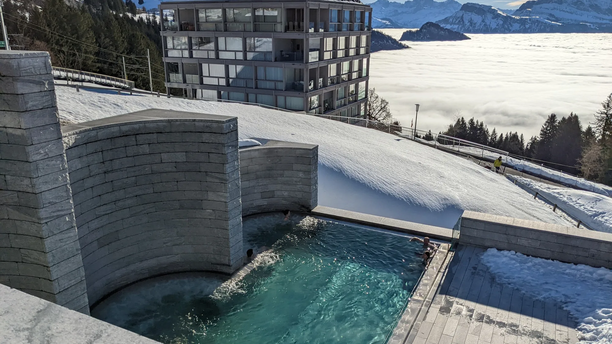 The outdoor pool of the Rigi Kaltbad mineral baths in the snow, behind it the sea of fog over the valley